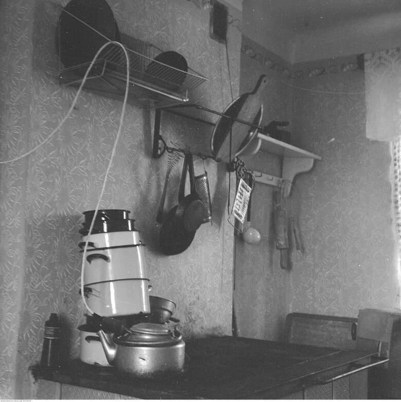 1970 rok. Kuchnia węglowa i sprzęty kuchenne zawieszone na hakach. Na kuchni widoczny aluminiowy czajnik z wetkniętą do wody grzałką nurkową.
