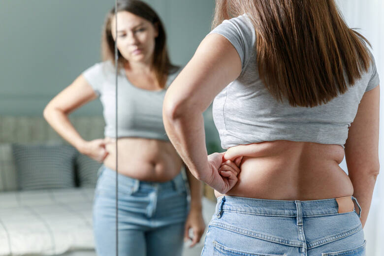 Młoda kobieta sprawdza fałdę tłuszczu przy lustrze