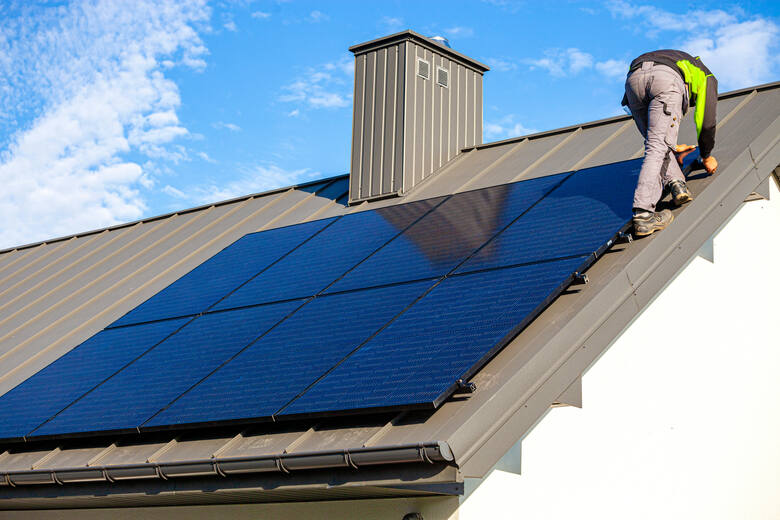 mężczyzna montujący panele słoneczne na dachu domu