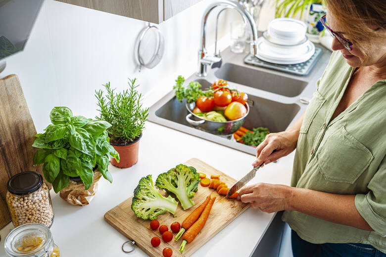 Kobieta w średnim wieku kroi warzywa na blacie w kuchni