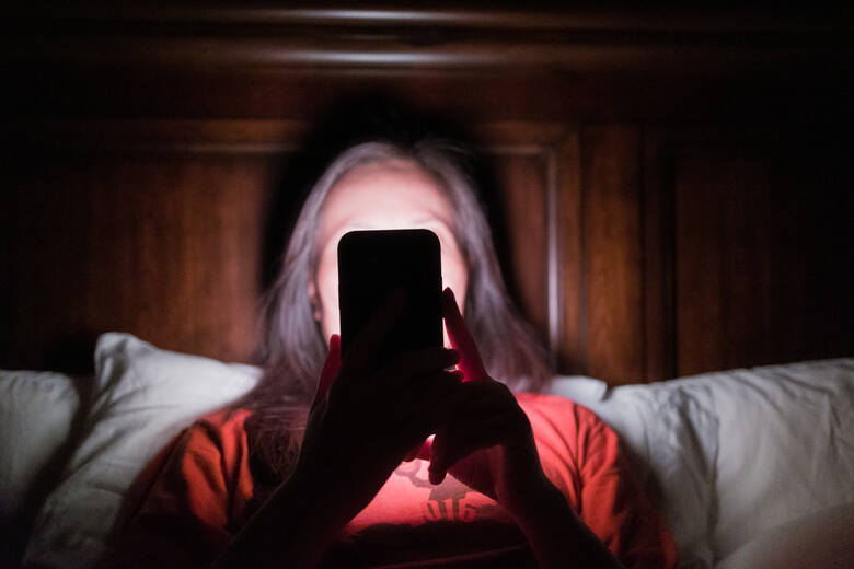Kobieta korzysta ze smartfona w nocy i zasłania twarz