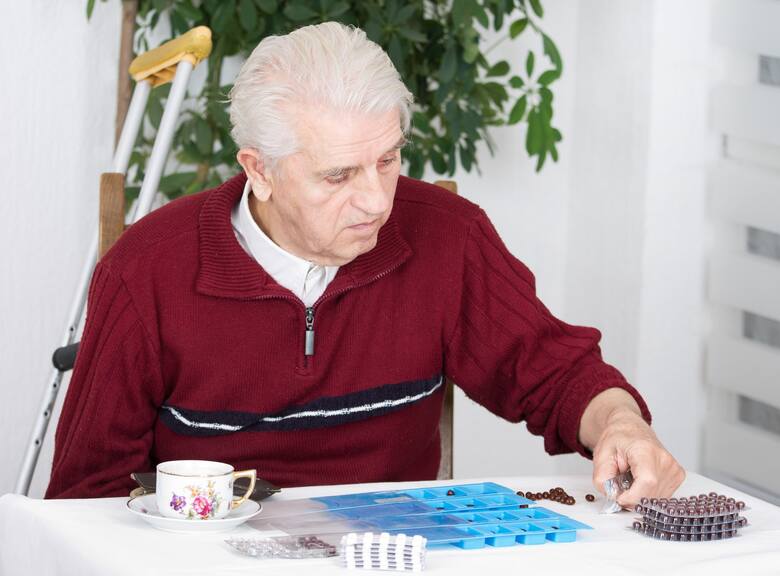 Starszy siwy mężczyzna rozdziela na stole leki w blistrach