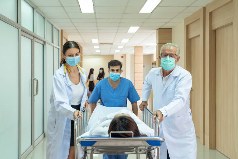 Personel medyczny wiezie pacjentkę na łóżku przez korytarz szpitala