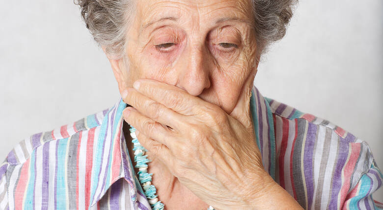 Starsza kobieta zasłania usta dłonią