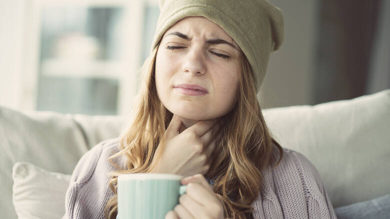 Młoda kobieta w czapce z bólem gardła i kubkiem herbaty