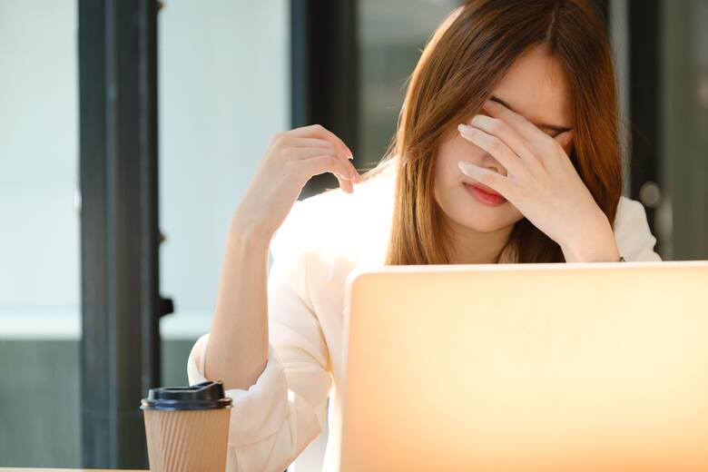 Młoda kobieta przed komputerem zakrywa oczy dłonią