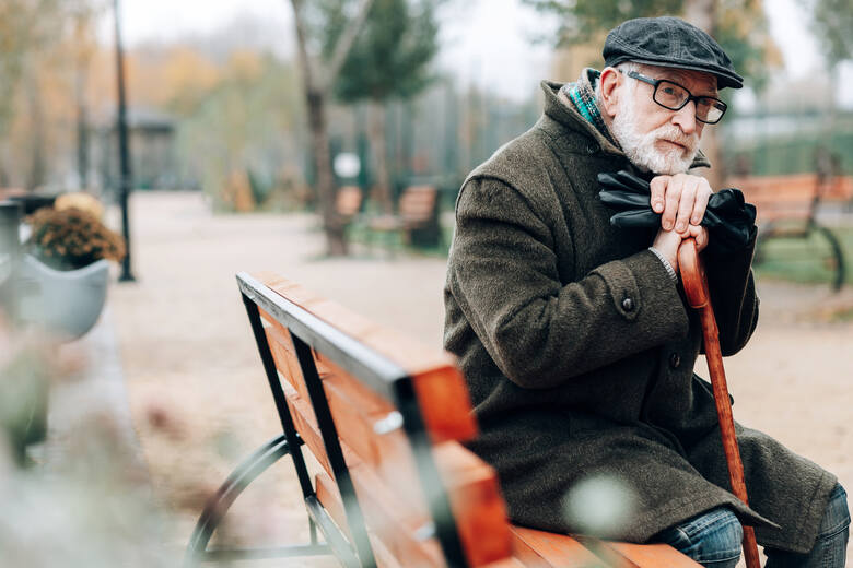 Starszy mężczyzna siedzi na ławce w parku, opierając się na lasce
