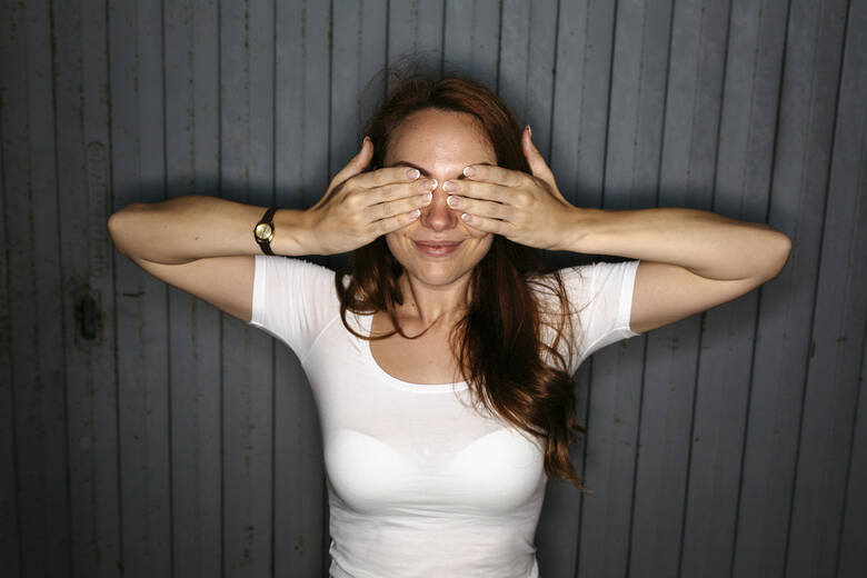 Młoda kobieta zakrywa oczy dłońmi