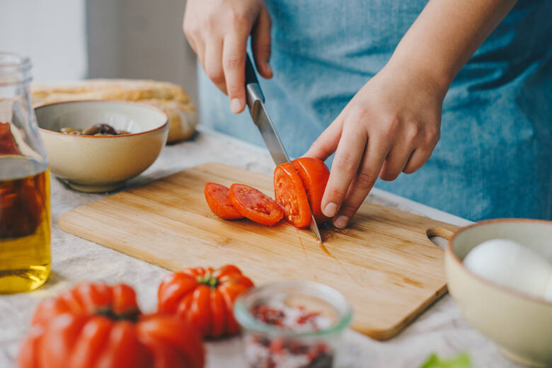 Krojenie pomidorów na desce i składniki sałatki na stole