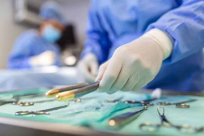 Pielęgniarka bierze do ręki narzędzie chirurgiczne dla grupy chirurgów w tle, którzy operują pacjenta