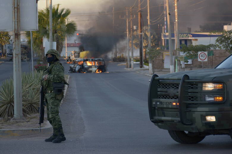 Żołnierz na tle scenerii walk. Na dalszym planie jeden z samochodów podpalonych po starciach sił policyjnych z gangami w mieście Culiacan w stanie Sinaloa