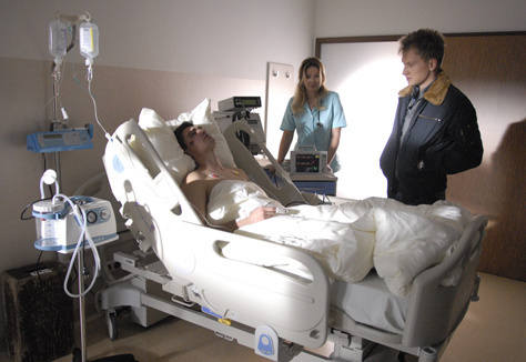 Komisarz Bromski przesłuchuje ofiarę wypadku motocyklowego. Nad bezpieczeństwem pacjenta czuwa lekarka (w tej roli Marta Dąbrowska). 