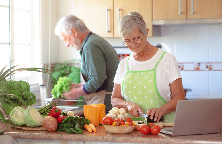 Para starszych ludzi przygotowuje wspólnie posiłek z warzyw