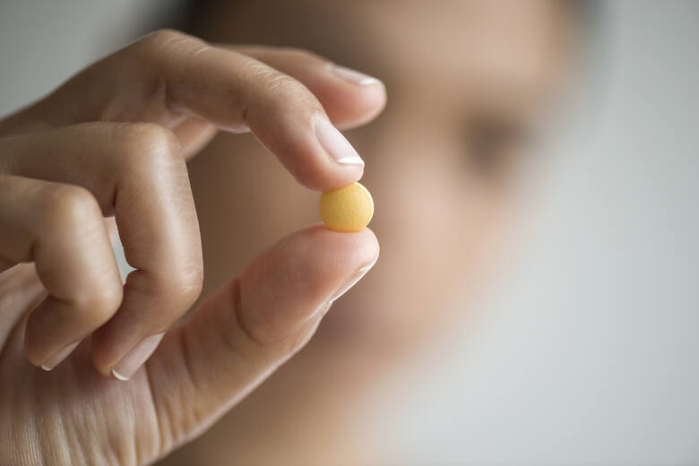 Mała żółta tabletka w palcach ręki