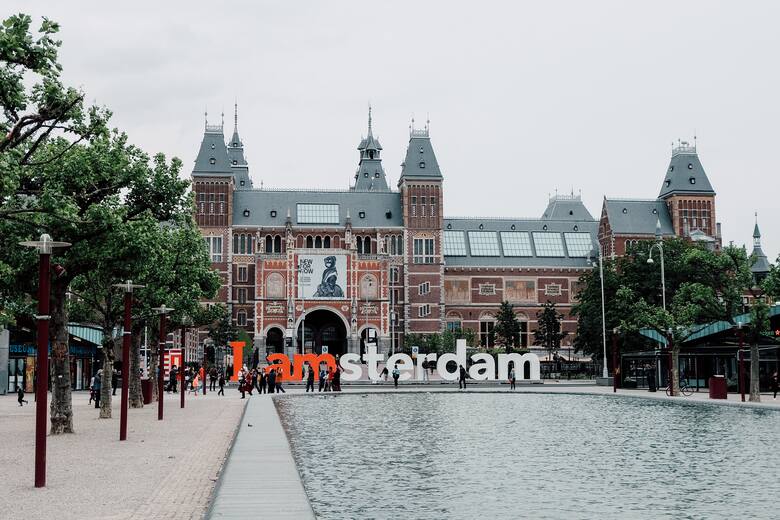 Ludzie na tle budynku i napisu promocyjnego miasta Amsterdam