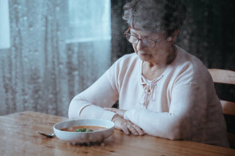 Samotna starsza kobieta siedzi nad zupą. 