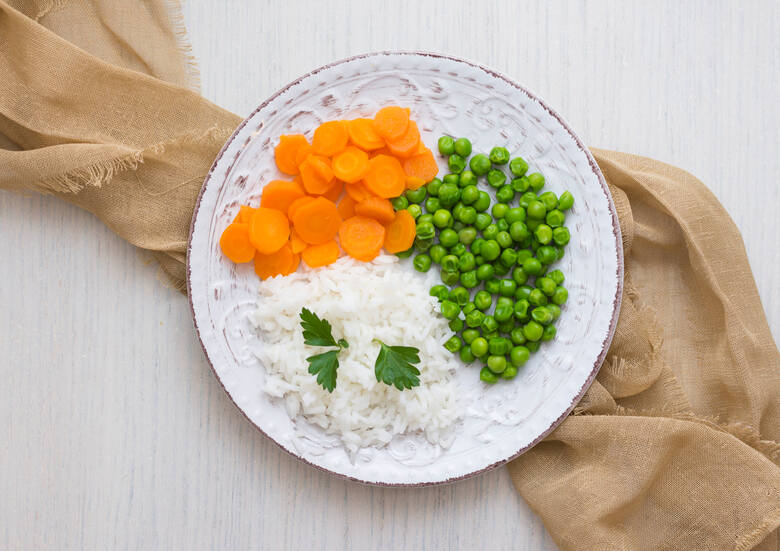 Widok na talerz od góry: gotowany biały ryż, groszek i marchewka