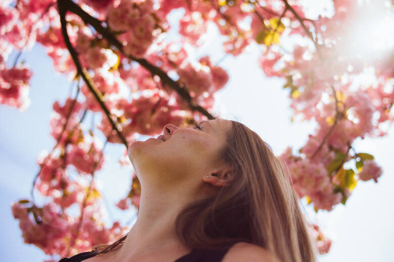 Młoda kobieta wącha różowe kwiaty na drzewie