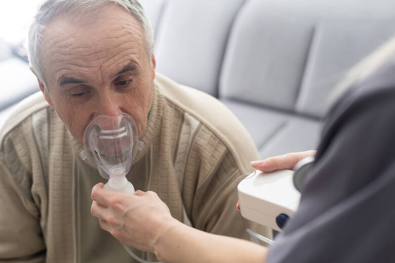 Starszy mężczyzna z maską na ustach i koncentratorem tlenu
