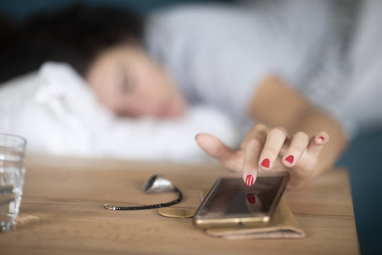 Kobieta w łóżku wyłączająca alarm w telefonie komórkowym
