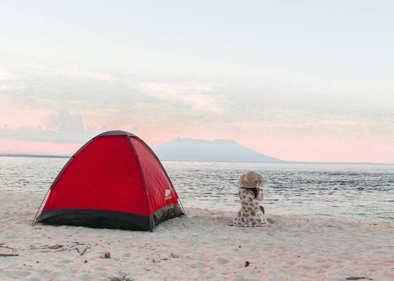 Kobieta siedząca na plaży obok namiotu