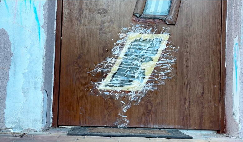 Do domu, w którym rozegrała się tragedia, prowadzą zniszczone drzwi. Ktoś zakleił dziurę zwykłą taśmą klejącą.