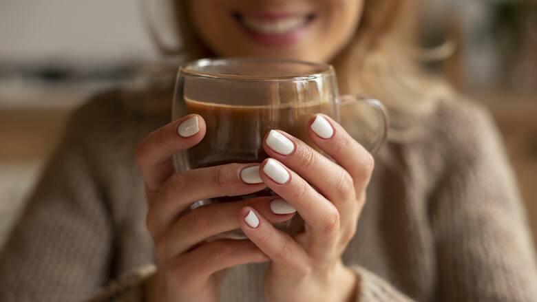 Kobieta trzyma w dłoniach szklankę z kawą