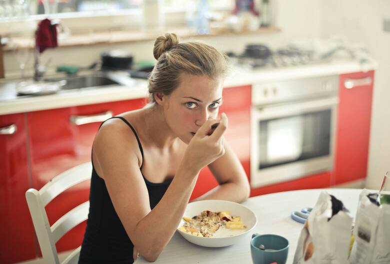 Młoda kobieta przy śniadaniu w kuchni je płatki z mlekiem