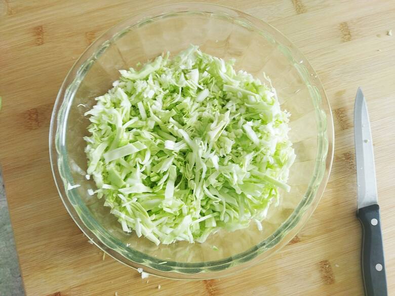 Przełóż posiekaną kapustę do salaterki i posól. Całość wymieszaj i odstaw na chwilę na bok.