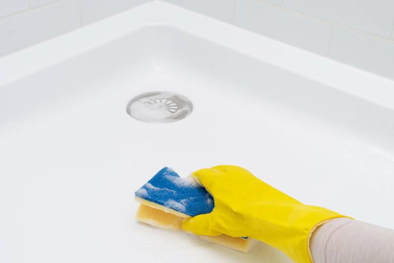 ręka w gumowej rękawiczce myjąca brodzik za pomocą gąbki i deteregntu