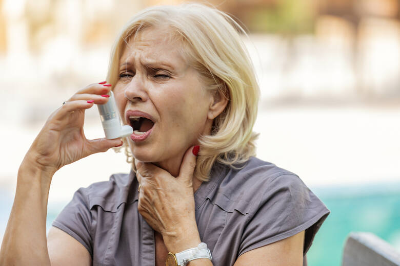 Kobieta w średnim wieku z napadem astmy trzyma w dłoni inhalator