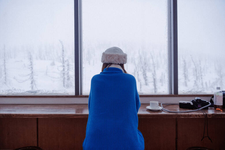 Kobieta wpatrzona w zimowy krajobraz za oknem