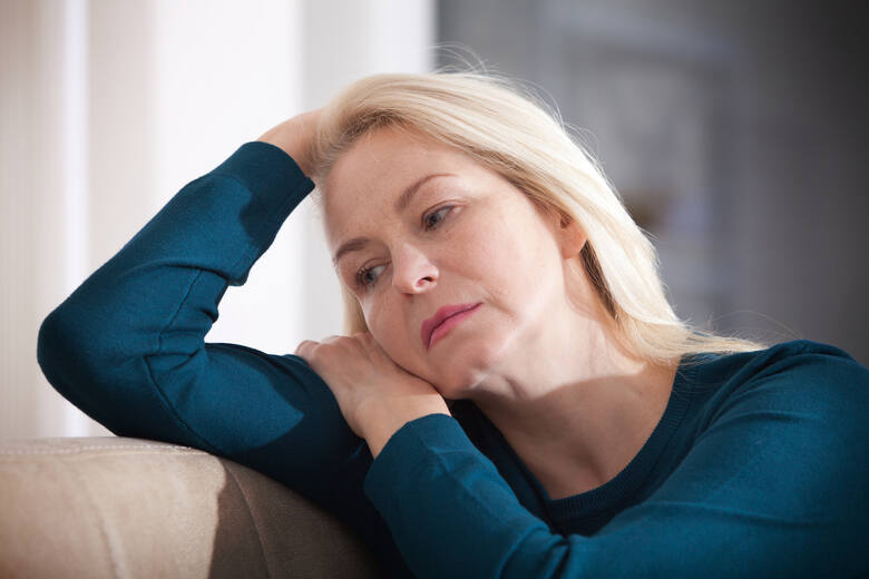 Kobieta w średnim wieku siedzi zmęczona i w smutnym nastroju