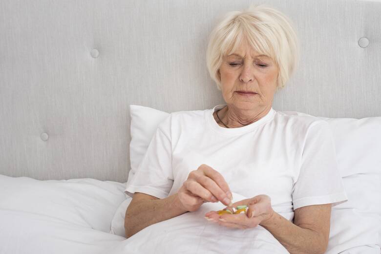Starsza kobieta w łóżku zażywa leki