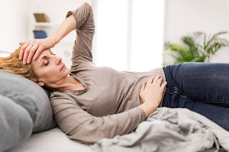 Zmęczona kobieta z problemami żołądkowymi leżu w domu na kanapie