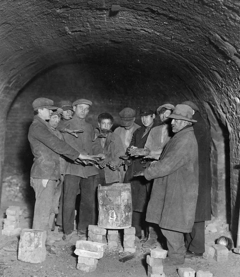 Grupa bezrobotnych mężczyzn podczas ogrzewania się w korytarzu starej cegielni pod Katowicami