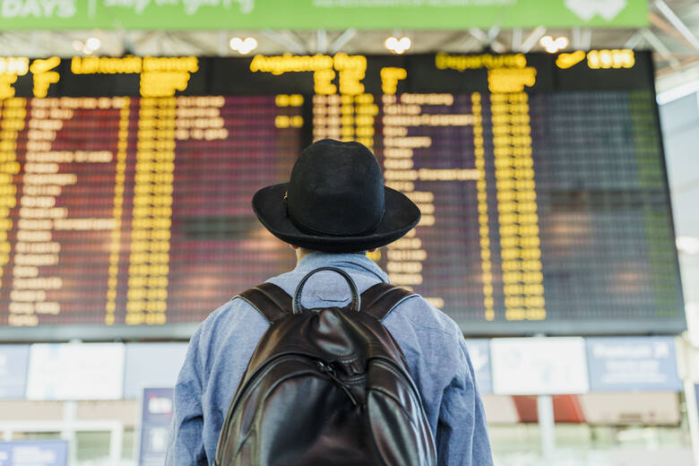 Mężczyzna patrzy na tablice odlotów i przylotów na lotnisku