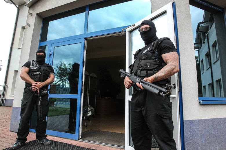 Uzbrojeni po zęby i zamaskowani ochroniarze firmy Rutkowski Patrol strzegą wejścia do budynku.