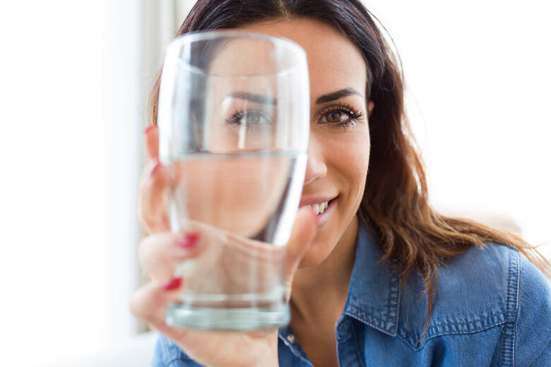 Młoda kobieta trzyma przed twarzą szklankę z wodą