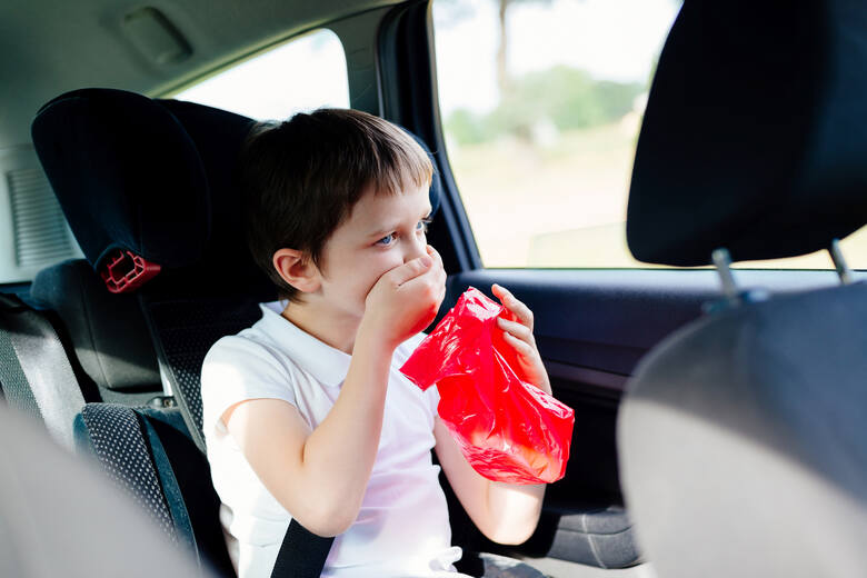 Chłopiec z chorobą lokomocyjną w samochodzie z czerwoną torbą w ręku