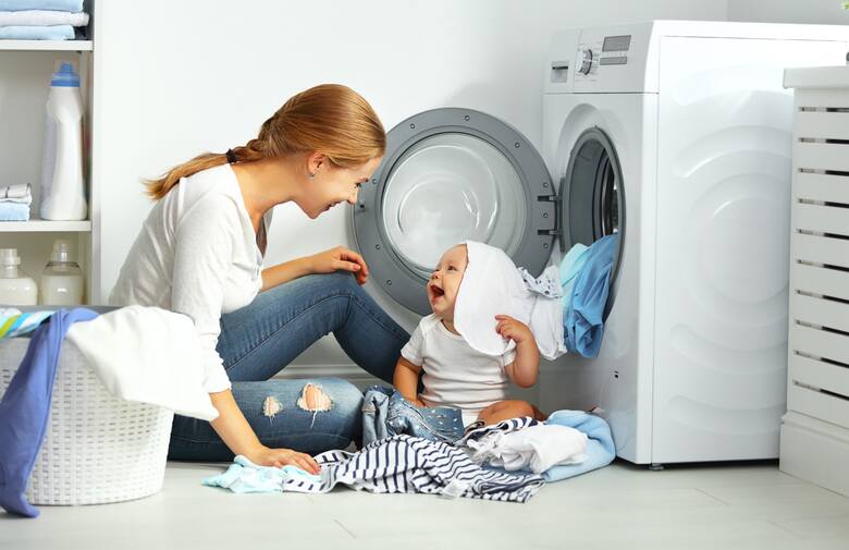 Kobieta bawi się z dzieckiem przy pralce.
