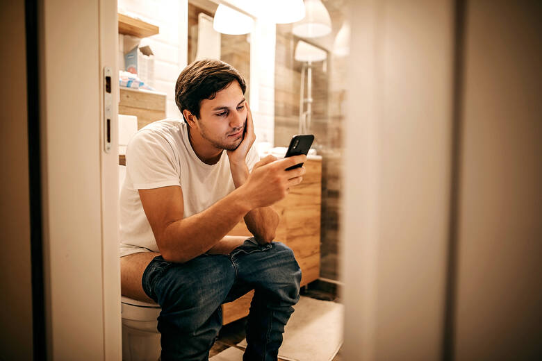 Mężczyzna siedzi na toalecie i przegląda telefon