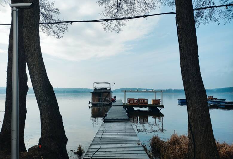 Widok na Jezioro Ukiel z plaży należącej do Hotelu Pirat. Przy pomoście zacumowany boathouse, w którym można spędzić noc lub popływać po jeziorze.