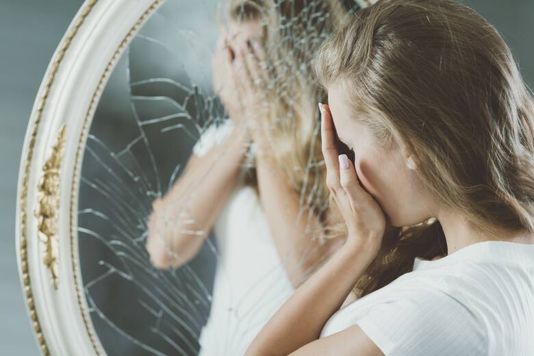 Młoda kobieta z problemami psychicznymi przy rozbitym lustrze