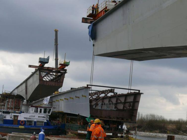 Najpierw do przęsła znajdującego się na barce zamontowano osiem prętów, przy pomocy których ostatnia część mostu została podniesiona