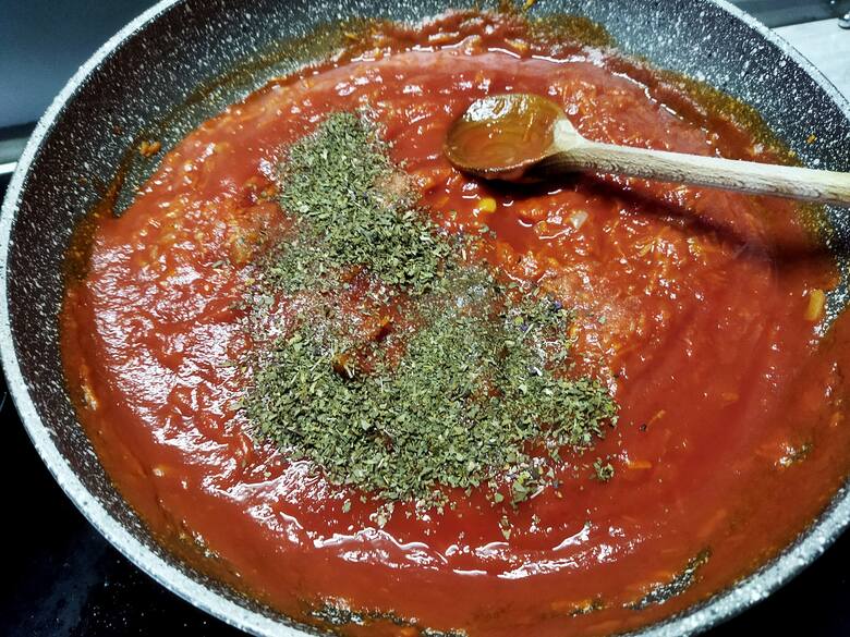 Dodaj bazylię, oregano, ostrą paprykę, sól i pieprz. Dopraw do smaku.Gotuj sos jeszcze ok. 1 min.