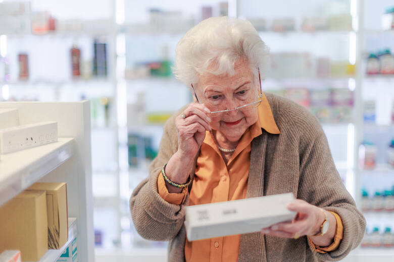 Seniorka czyta ze zdziwieniem informacje na opakowaniu leku