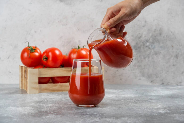 Ręka nalewająca do szklanki sok pomidorowy, w tle skrzyneczka pomidorów