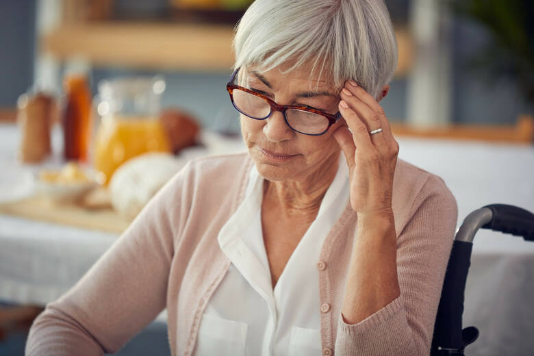 Starsza kobieta przy stole z bólem głowy dotyka skroni dłonią