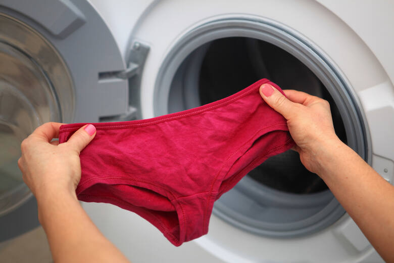 Osoba trzymająca w dłoniach czerwone majtki przed bębnem pralki